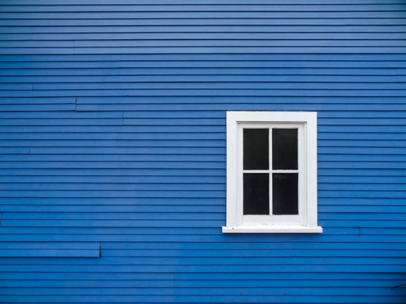 A single white-paned window on a blue wall of a house