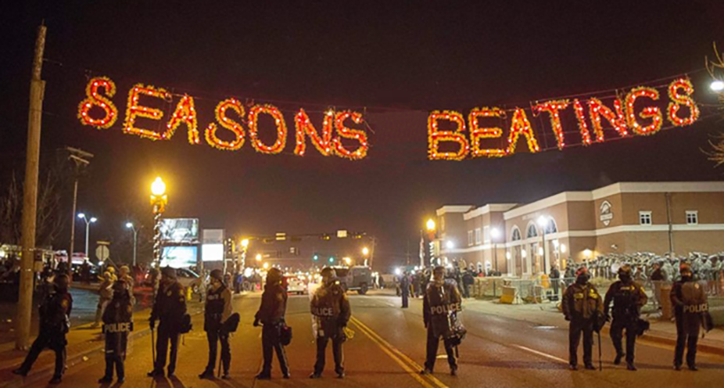 Picture of police in riot gear standing under lights that read "Seasons Beatings"