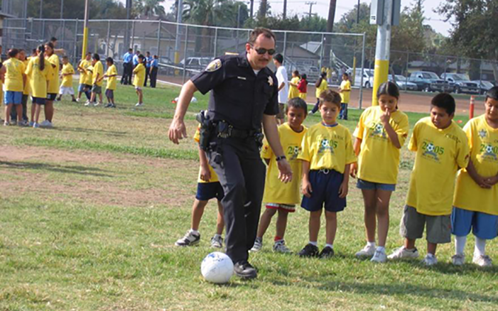 Picture of police officer kicking a soccer ball with local children